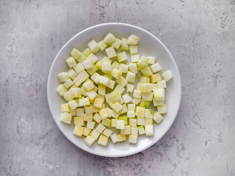 Top view of white plate with brunoise zucchini on a gray background.