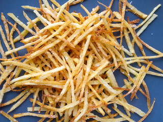 Top view of hot fried potato sticks on a bright blue plate. Delicious salty snack.