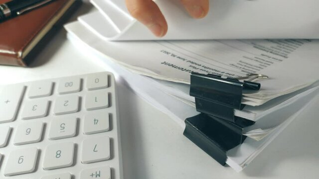 Front view of a Businessman hand searching documents files or information in Stack of financial report papers folder on work in office table