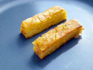 Side view of two fried potato gratin pieces on a plate.