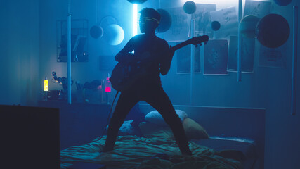 Pan around view of male teenager in glowing sunglasses playing loud music on electric guitar while...