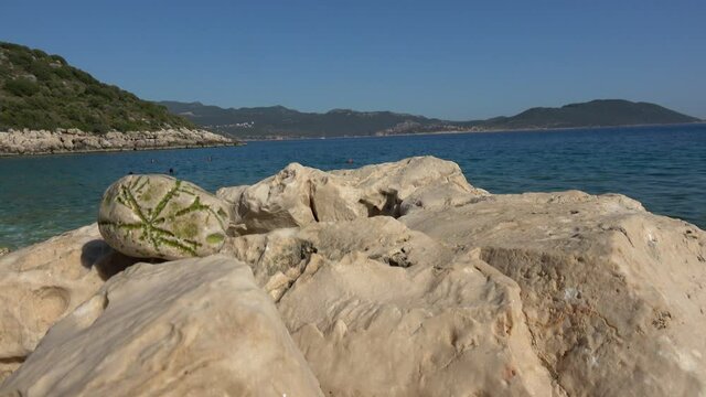 Kas, Turkey - 27th of May 2021: Criptic stone on rocks and people swimming in the background
