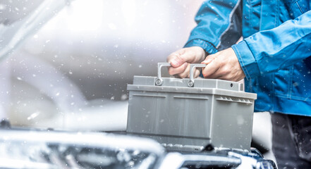 Car technician replaces dead car battery in winter conditions - obrazy, fototapety, plakaty