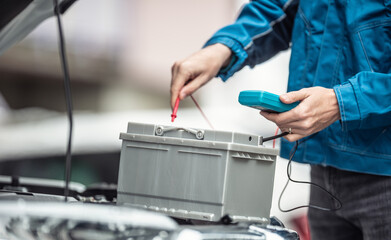 Car repaid garage technician checks lifespan of a car batery with a multimeter