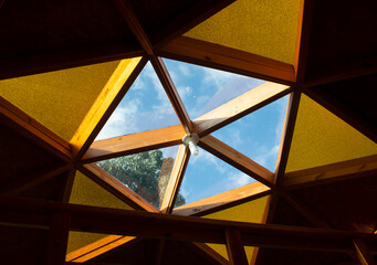 Pentagonal transparent window to observe stars into a wooden glamping with triangular yellow glass windows