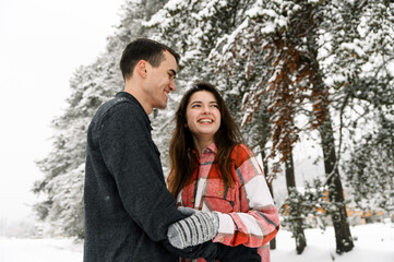 Fototapeta premium Loving couple in shirt on a winter walk. Man and woman having fun in the frosty forest. Romantic date in winter time.Christmas mood of a young family.Winter lovestory