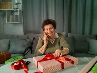 Elderly woman packing gifts and talking on the phone