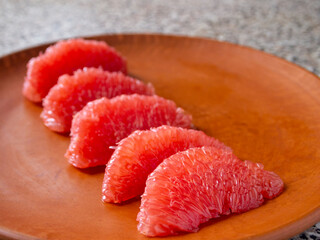 Peeled grapefruit slices side view. Appetizing fruit on a brown clay plate.