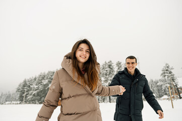 Loving couple in puffer jacket on a winter walk. Man and woman having fun in the frosty forest. Romantic date in winter time.Christmas mood of a young family.Winter lovestory