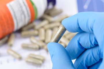 Supplement capsule in scientist hands, with bottle and pills on background.