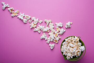 Small green bucket of pop corn on pink background. Some popcorns lying near. Copy space. Top view.