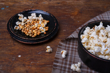 Heap of ready and raw popcorn in black bowl on wooden rustic background. Some popcorns on fabric and table