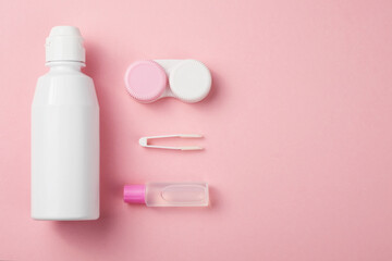 Contact lens accessories: solution, container, tweezers. Pink background, copy space.