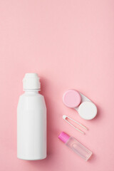 Contact lens accessories: solution, container, tweezers. Pink background, copy space.