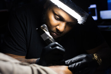 Tattoo artist is concentrated on his work at tattoo studio. Close up.
