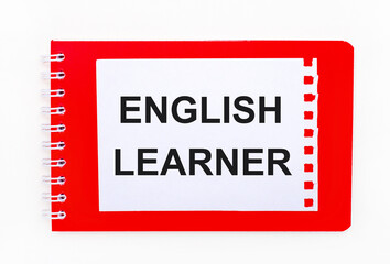 On a white background - a bright red notebook on a spiral. On it is a white sheet of paper with the text ENGLISH LEARNER
