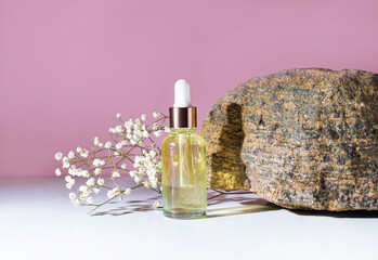 On a light pink background there is a transparent bottle with light yellow oil and a place to...