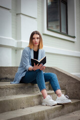 A business girl with a notebook sits on the steps. Businesswoman. Business style. Student. Psychologist. Thoughtful