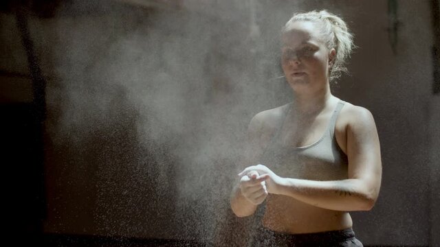 Medium shot of athlete clapping hands with magnesia powder. Chalk powder exploding into dust particles in sunlight. Powerful woman getting ready for boxing training. Sport, kickboxing concept