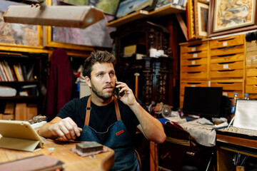 Young Caucasian man talking on the phone in his jewelry workshop. picking up work orders.