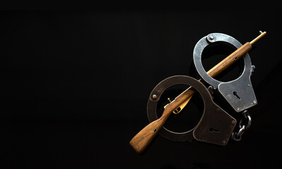 Miniature of a wooden rifle. Metal handcuffs with a gun. Arms trafficking. Gun laws.Black background for the text of criminal news.