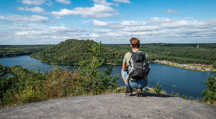 Young male backpacker squatting on a rock and enjoying the beautiful panoramic landscape.