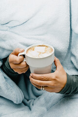 close up of an unrecognizable woman covered in blankets holding a cup of hot chocolate with marshmallows