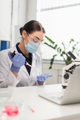 Scientist in latex gloves and medical mask working with petri dish and electronic pipette in lab.