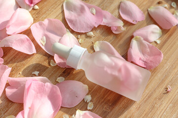 Clear bottle with pure rose essence oil and white dropper lying on a wooden background. Mock up idea