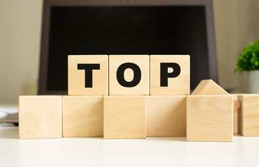 The word TOP is written on wooden cubes lying on the office table in front of a laptop.