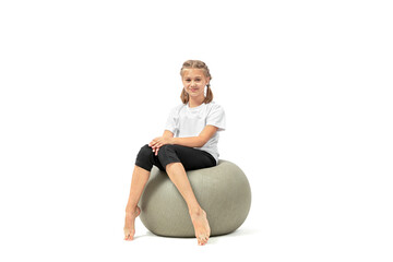 Cute young girl sitting on fitness ball looking at the camera and smiling isolated on white background.