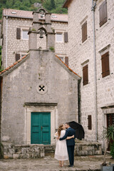 Fototapeta na wymiar Groom embraces bride near the green door of the ancient church. Back view
