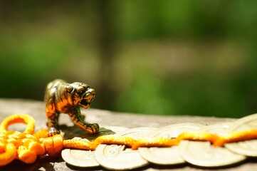 A metal tiger figurine and a bunch of Chinese coins on a tree branch.