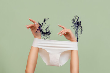 Female's hands, which hold dry plants, arms are wearing white panties. Green background. The...
