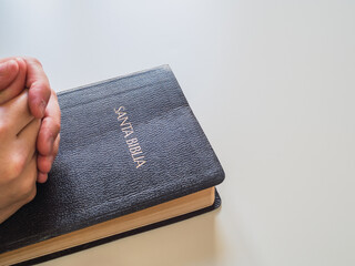 Hands linked on holy bible with copy space on white background. The book says in Spanish: Holy Bible