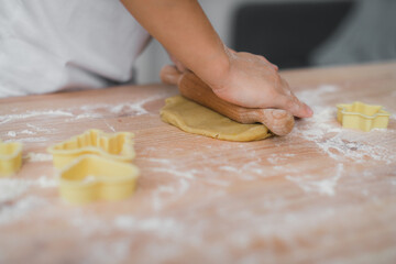 Close-up of a child's hand roll out the dough with a wooden rolling pin. Child working with raw pastries, making cookies.