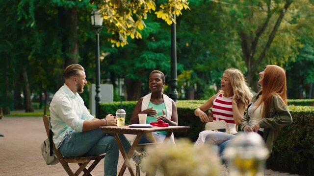 In the middle of the park at the cafe black woman very charismatic and other blonde hair guy with their friends all together have a meeting they discussing with each other and enjoy the time