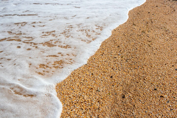White foam wave on the background of a sandy beach