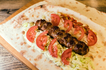 Shawarma with meat kebabs, with sauce, tomatoes, peppers, cheese, herbs, cabbage, onions and garlic on ruddy pita bread, lying on a wooden board