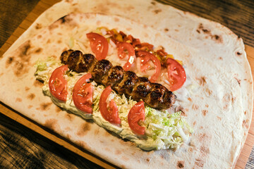 Shawarma with meat kebabs, with sauce, tomatoes, peppers, cheese, herbs, cabbage, onions and garlic on ruddy pita bread, lying on a wooden board