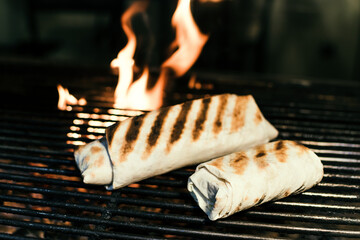 Shawarma with meat kebabs, on charcoal, on a fire, on a grill wire rack, with sauce, tomatoes, pepper, cheese, herbs, cabbage, onion and garlic in a ruddy pita bread, dark background