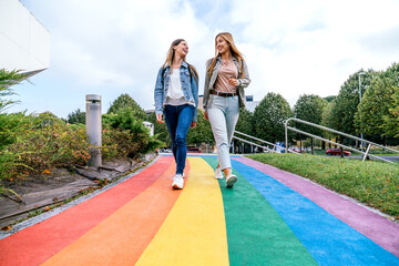Two women walking on a path painted with the colors of the rainbow while talking together.