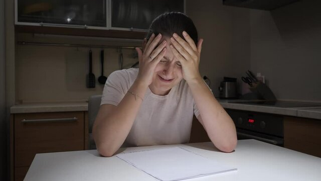 Upset stressed woman crying on kitchen at night after getting bad news and reading documents. Concept of financial difficulties, bankruptcy, taxes and rent payment.