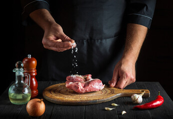 Chef sprinkles the meat with salt. Preparing meat before baking. Working environment in restaurant kitchen