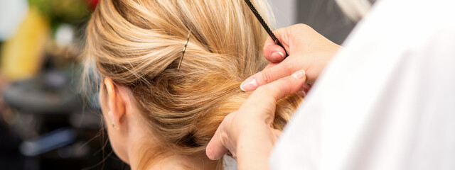 Naklejka premium Close-up hairdresser styling blonde hair on the back of the head in a beauty salon