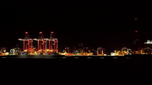 Panning shot of illuminated red cranes of Port Liverpool 2 and city skyline at night.
