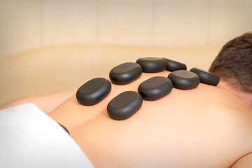 Hot stone massage therapy. Caucasian young man getting a hot stone massage on back at spa salon
