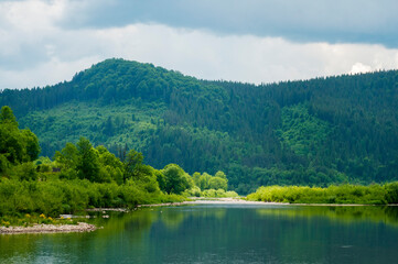 Mountain river surrounded by green trees, calm water.