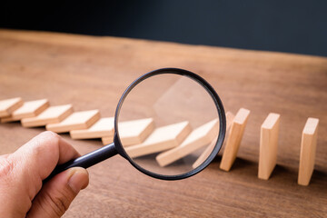 Closeup hand with a magnifying glass to look at the crash of domino, business recovery