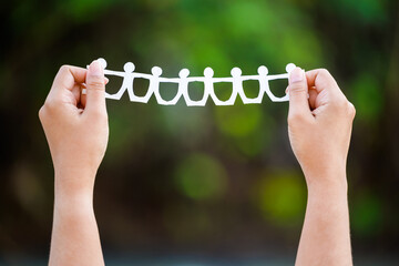 Woman's hand with paper chain doll on green forest background